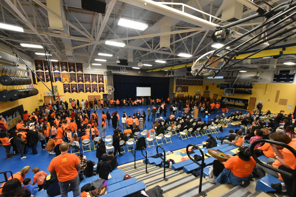 large gathering of people in gym wearing orange shirts standing in a circle