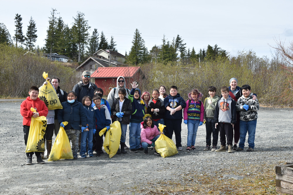 students and teachers smiling holding up yellow garbage bags on earth day