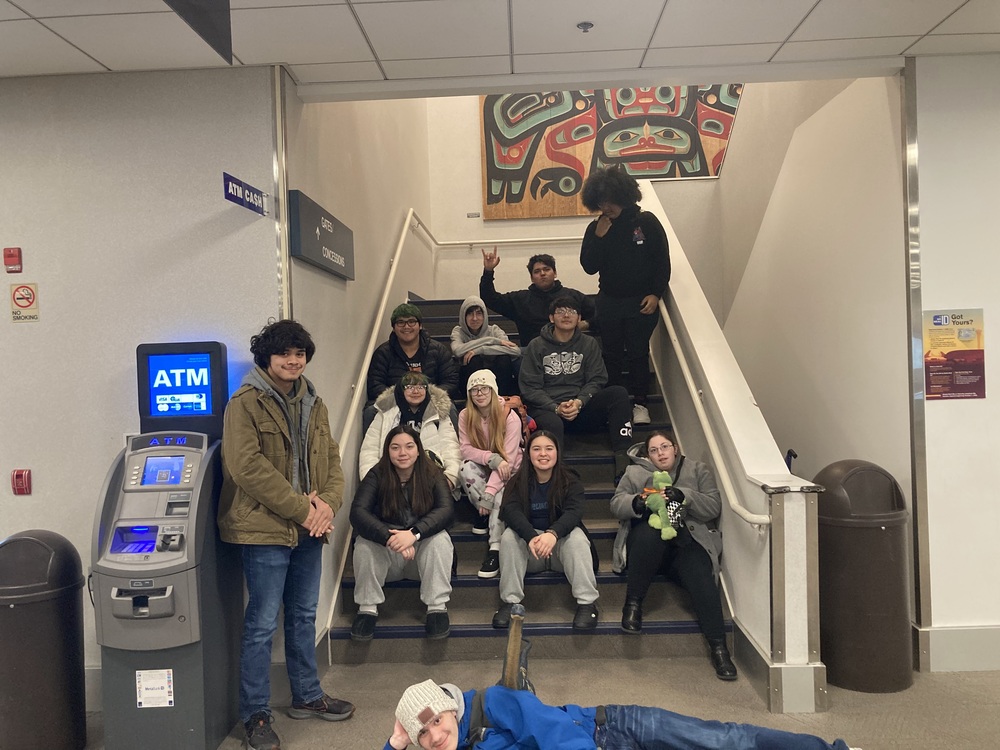 students smiling and sitting on stairs in an airport
