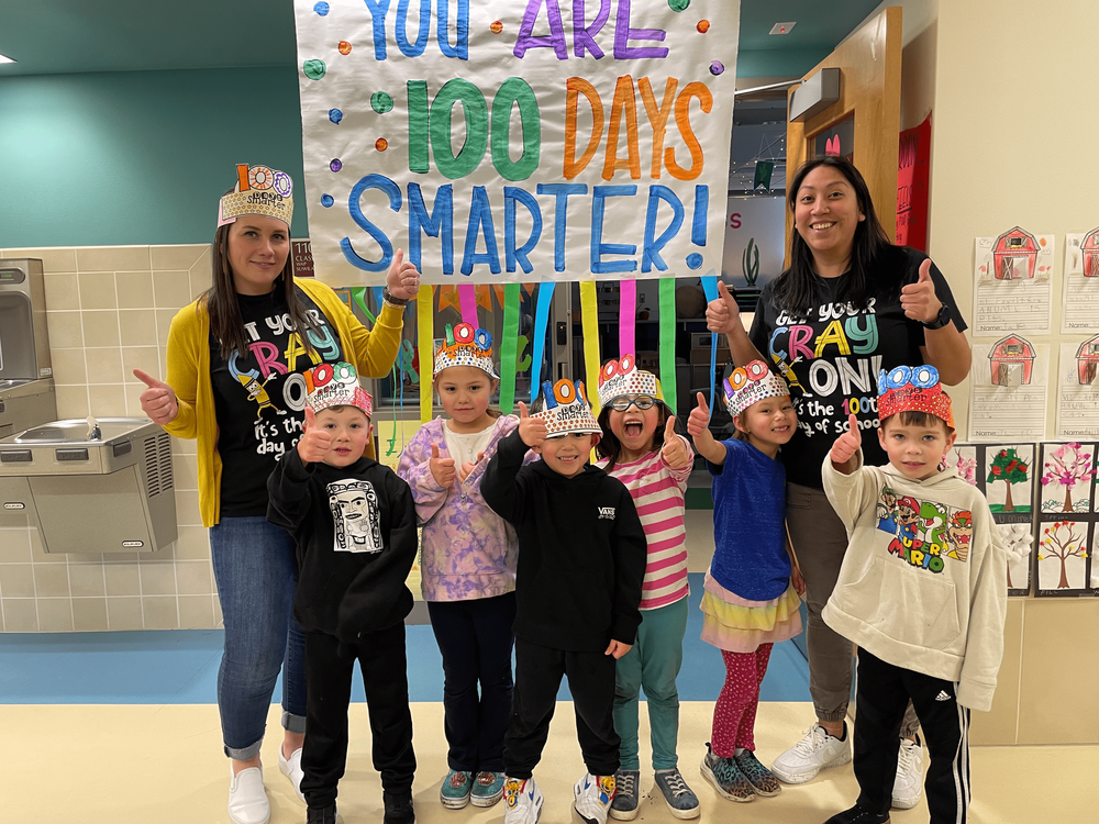 Students and teachers giving thumbs up in front of sign "You Are 100 Days Smarter!"