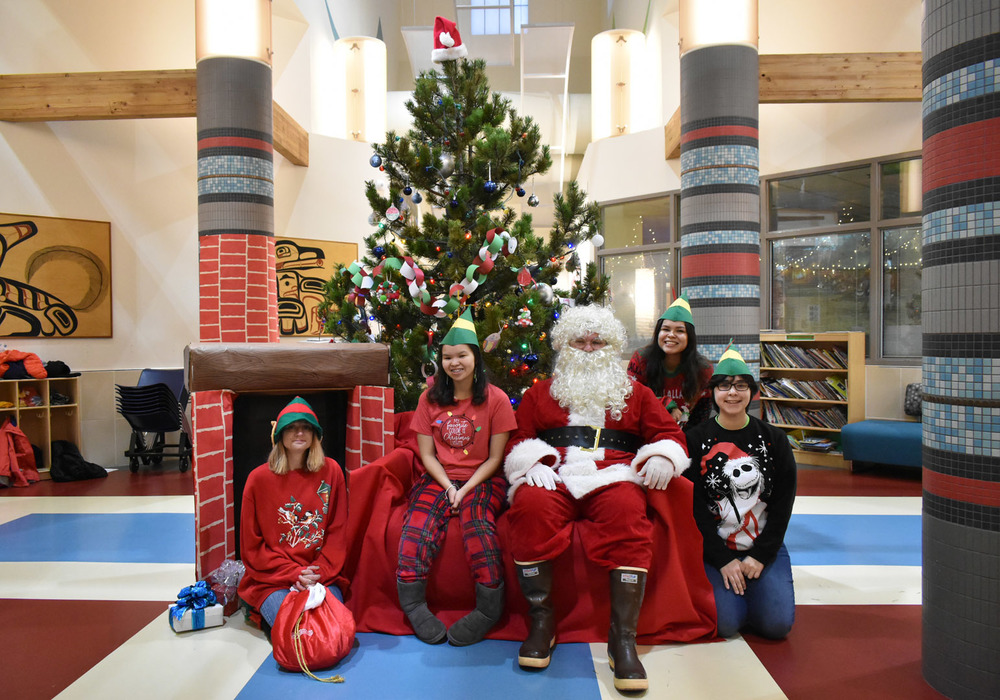 santa and elves sit in front of fireplace and tree at RJES