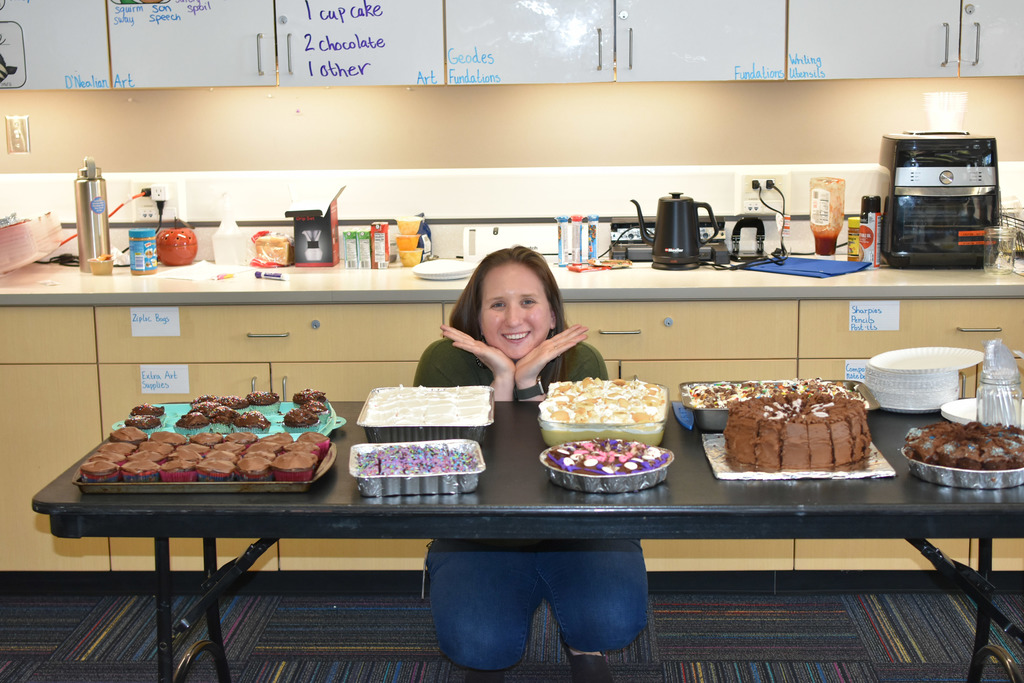 Mrs. Henry posing behind a table with the desserts made by students and staff