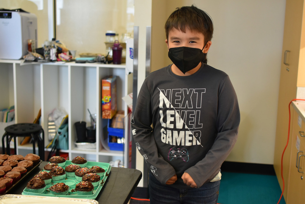 a student standing by cupcakes he made