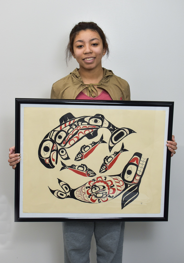 student holding artwork with a seal, salmon, and herring