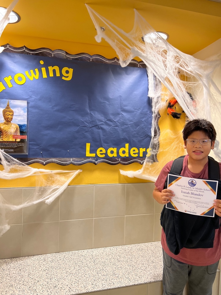 Picture of student holding a certificate next to a sign that says growing leaders