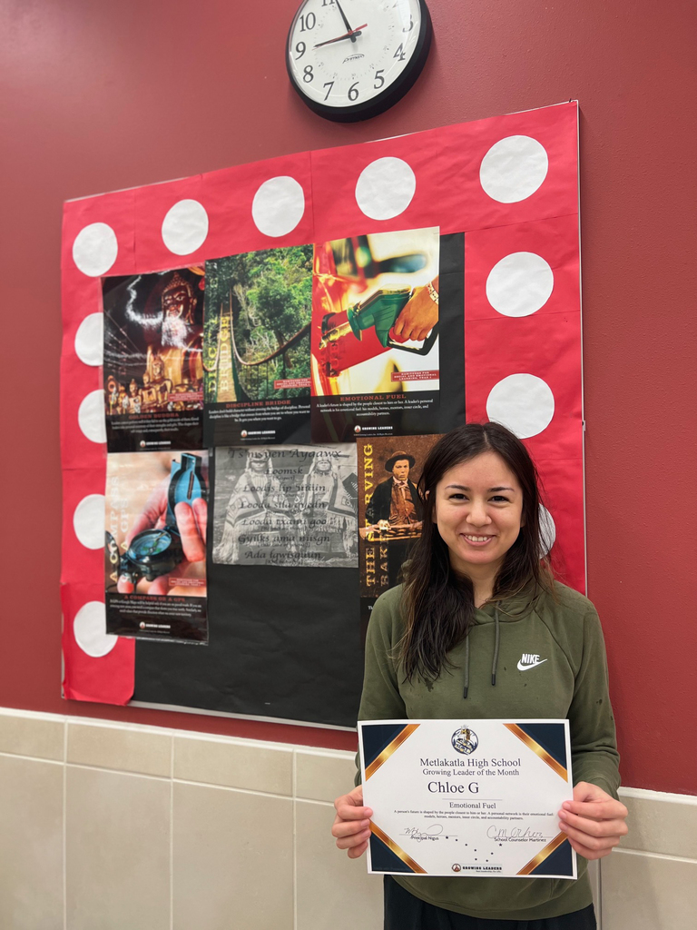 student smiling holding a certificate. Motivational posters in background.