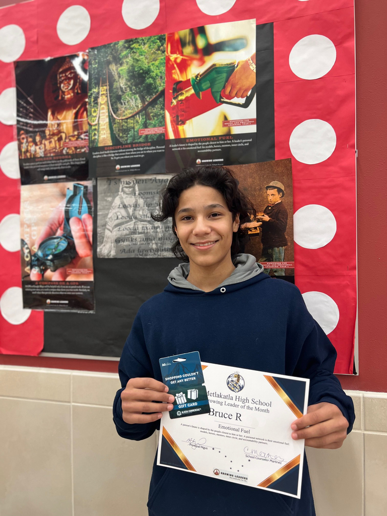 student smiling holding a certificate. Motivational posters in background.