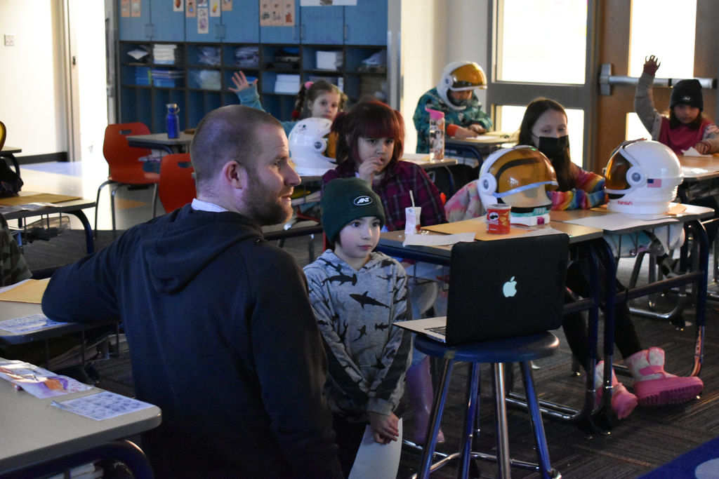 a student looking at a laptop while other students have space helmets on their desks
