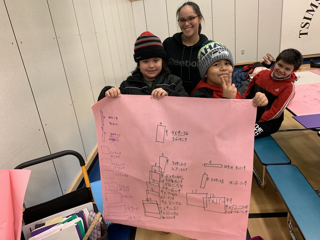 students holding up a poster with math problems smiling